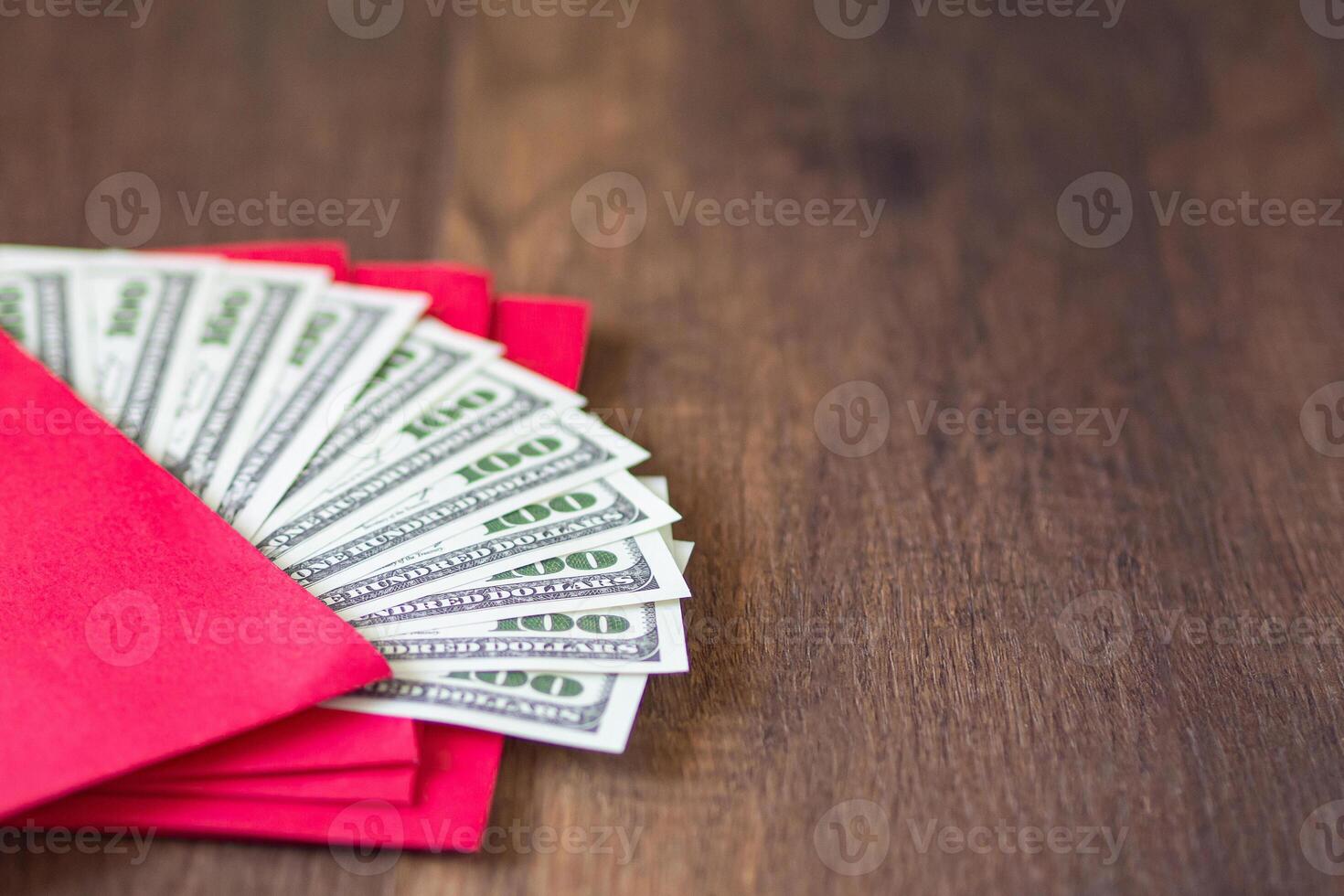 Close-up of red envelopes packet with US banknotes or Ang Pao prepare for giving to children in Chinese New Year. Wooden table background and space for text. Festival concept photo