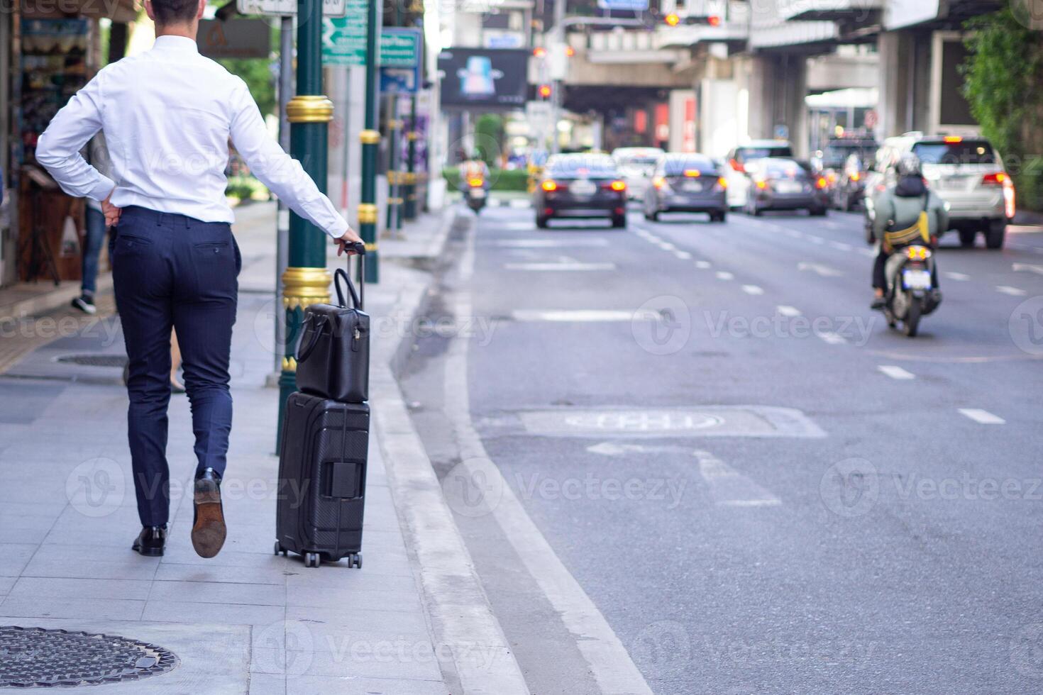 Back view of businessman walking pulling suitcase on the sidewalk. Traffic jams in the city. Lifestyle traveler young man holding baggage on street. Business journey travel. Business concept photo