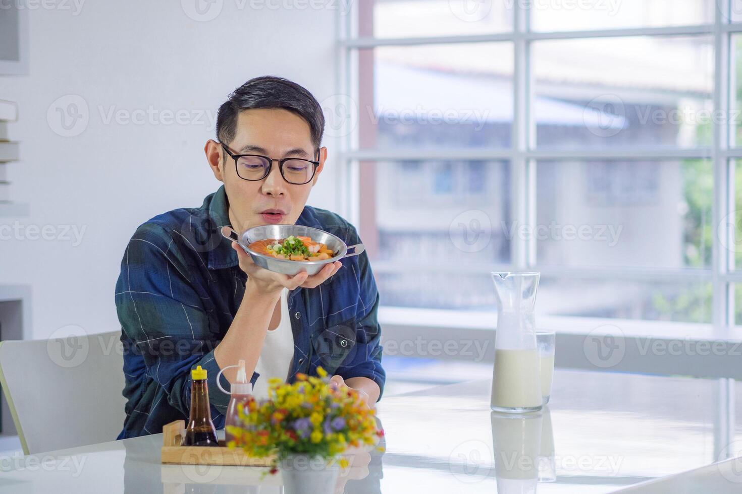 Young man wearing glasses sitting looking at the fried egg served on a pan with colorful toppings served on the pan egg. photo