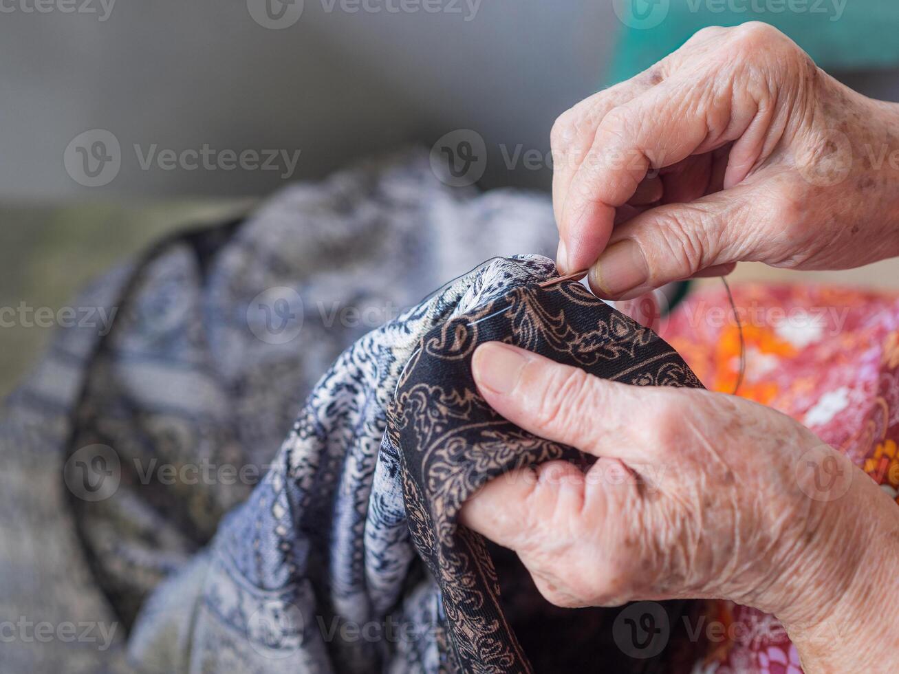 Close-up of hands senior woman using needle and thread to mend a pant. Selective focus. Concept of aged people and handmade photo