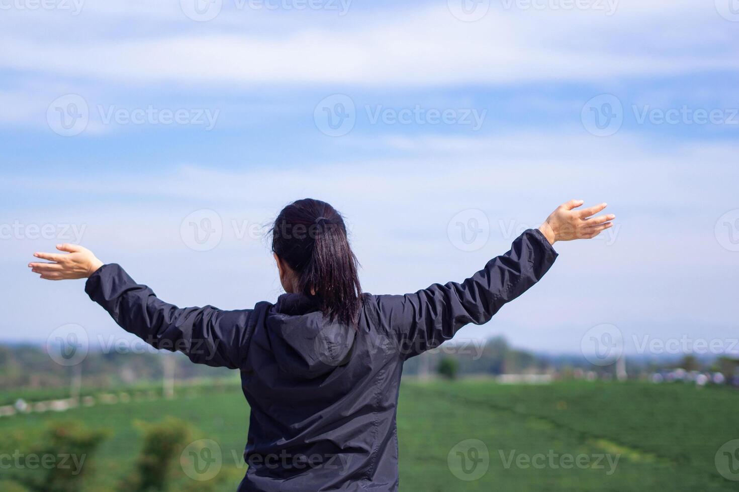 Back view of a woman hands up while standing looking at the tea plantation. Space for text. Relaxation concept photo