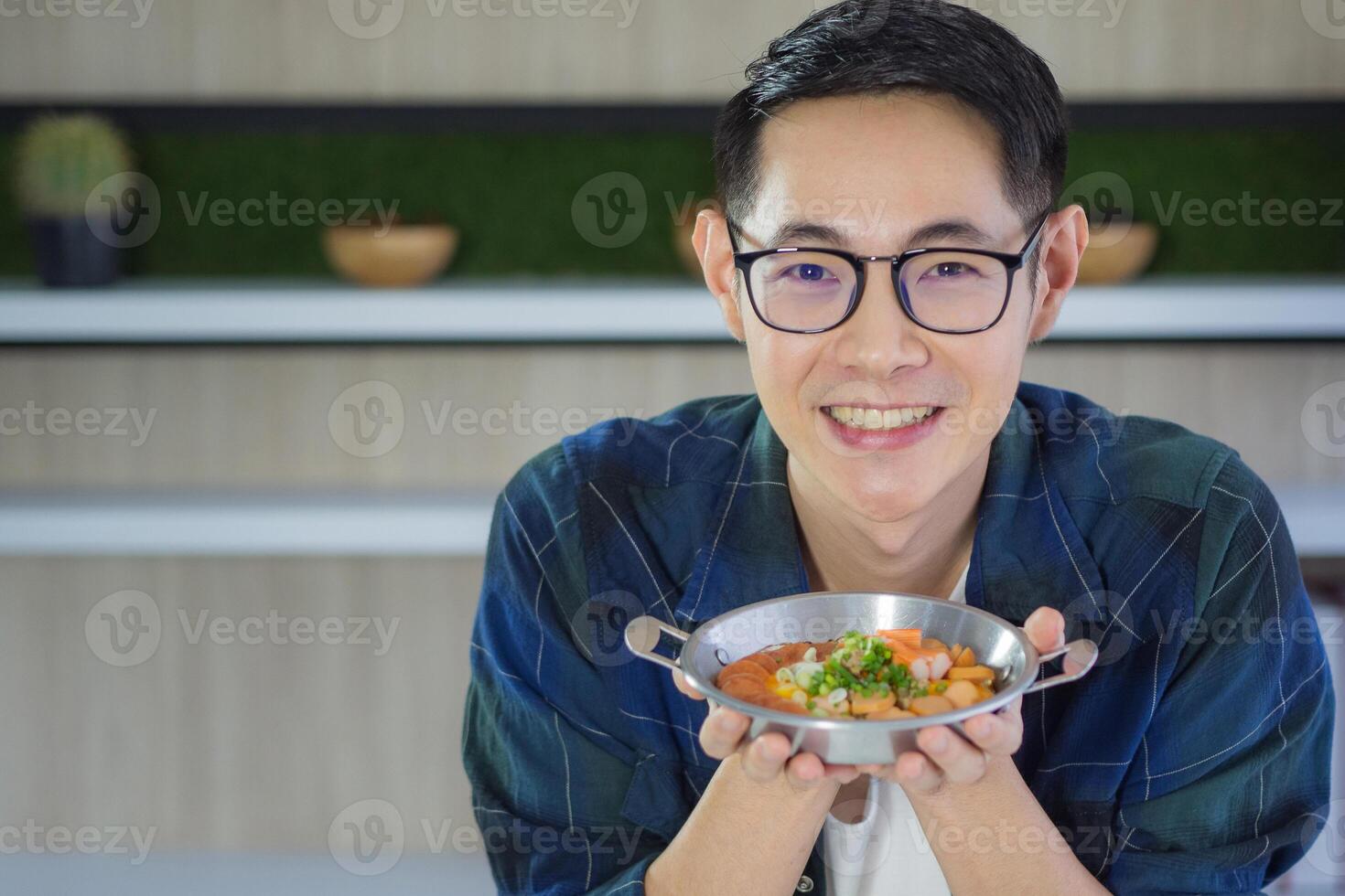 Young man wearing glasses holding a panned egg with colorful toppings served and looking at the camera. Space for text. Simple food for breakfast. Healthy foods concept photo
