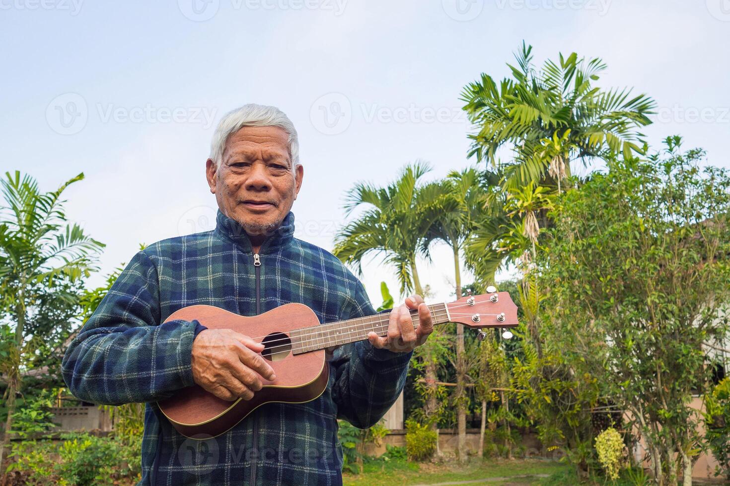 Portrait of a happy senior man playing the ukulele, smiling and looking at the camera while standing in a garden. Space for text. Concept of aged people and relaxation photo