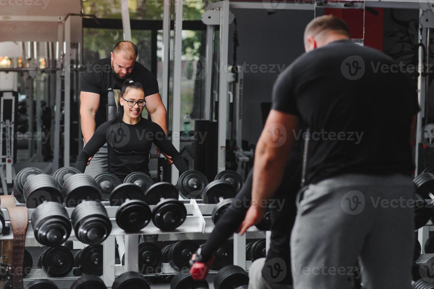 Beautiful girl with hands on dumbbells looking on her reflection in the mirror in a sports hall. Slim young woman is taking dumbbells in front of a mirror in fitness club photo