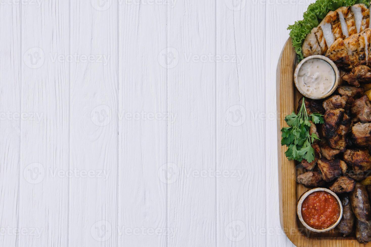 Most meat dish - beef kebabs, sausages, grilled mushrooms, potatoes, tomatoes and sauce. The best choice for a beer. Close-up on a white wooden background photo