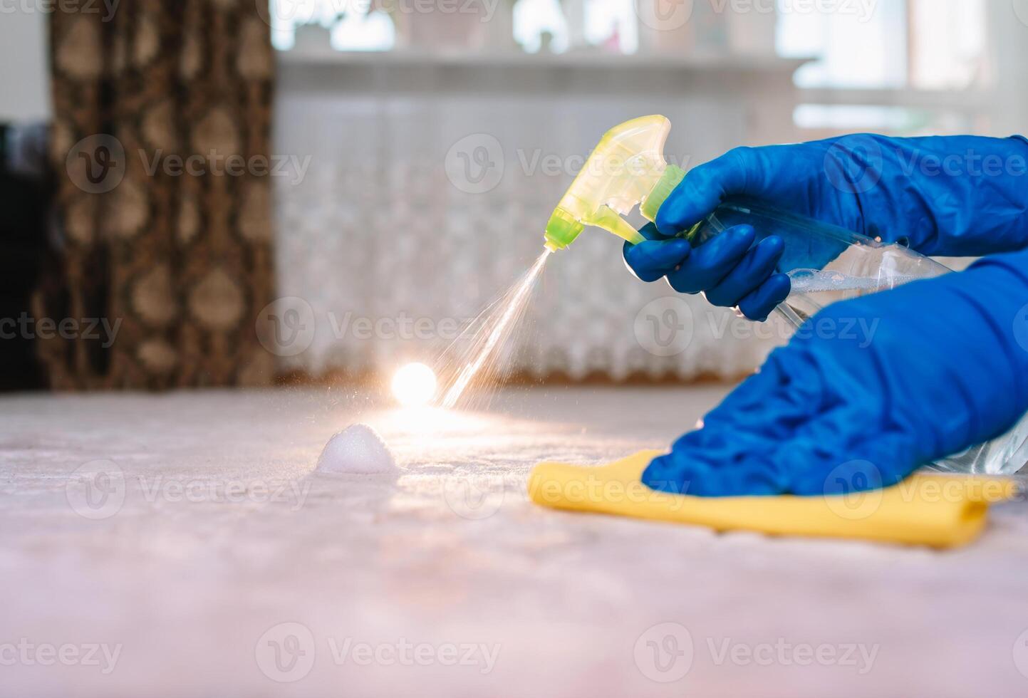 people, housework and housekeeping concept - close up of woman in rubber gloves with cloth and derergent spray cleaning carpet at home. close up of woman with cloth cleaning carpet photo