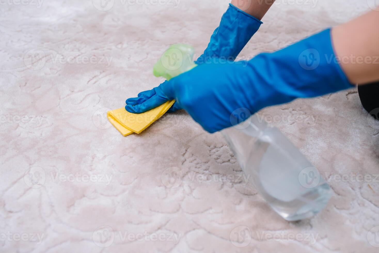 people, housework and housekeeping concept - close up of woman in rubber gloves with cloth and derergent spray cleaning carpet at home. close up of woman with cloth cleaning carpet photo