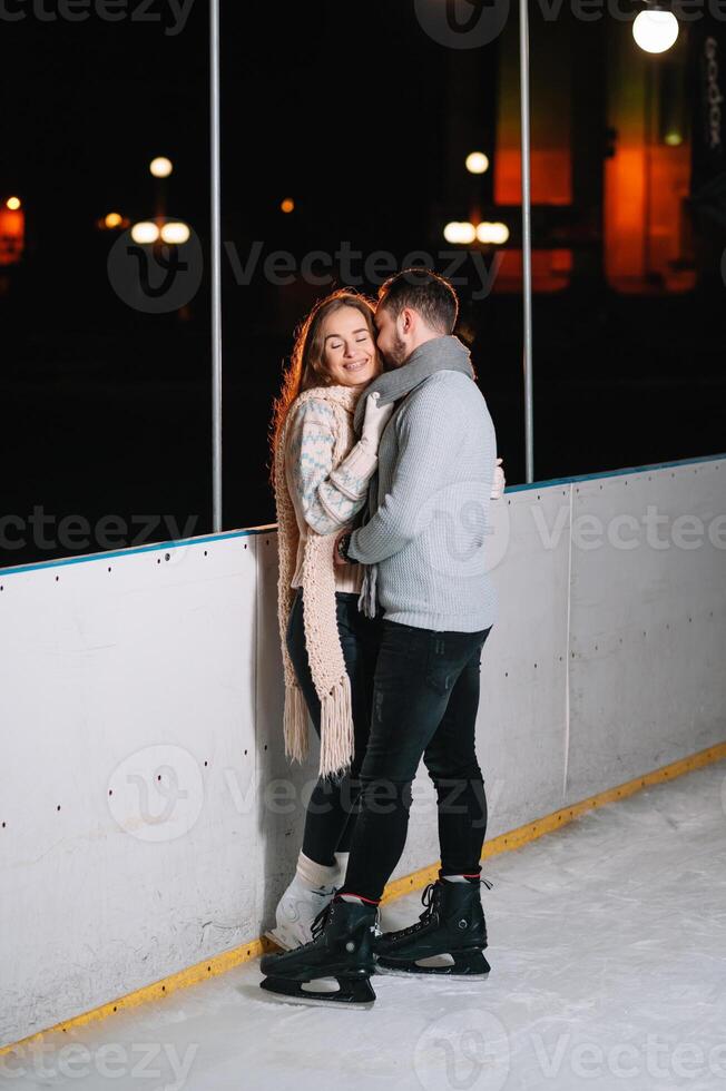 Theme ice skating rink and loving couple. meeting young, stylish people ride by hand in crowd on city skating rink lit by light bulbs and lights. Ice skating in winter for Christmas on ice arena. photo