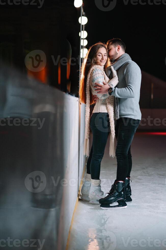 Theme ice skating rink and loving couple. meeting young, stylish people ride by hand in crowd on city skating rink lit by light bulbs and lights. Ice skating in winter for Christmas on ice arena. photo