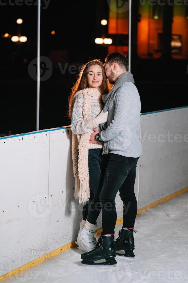 Theme ice skating rink and loving couple. meeting young, stylish people ride by hand in crowd on city skating rink lit by light bulbs and lights. Ice skating in winter for Christmas on ice arena. photo
