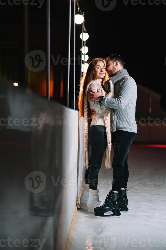 Theme ice skating rink and loving couple. meeting young, stylish people ride by hand in crowd on city skating rink lit by light bulbs and lights. Ice skating in winter for Christmas on ice arena. photo
