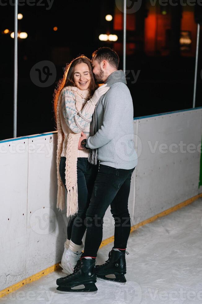 Theme ice skating rink and loving couple. meeting young, stylish people ride by hand in crowd on city skating rink lit by light bulbs and lights. Ice skating in winter for Christmas on ice arena. photo