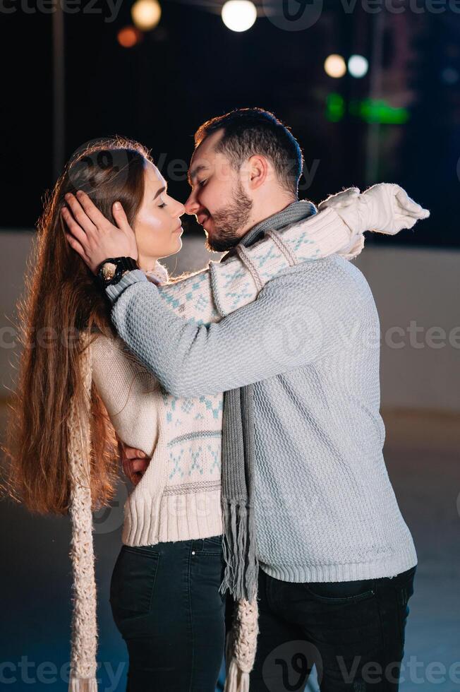 Theme ice skating rink and loving couple. meeting young, stylish people ride by hand in crowd on city skating rink lit by light bulbs and lights. Ice skating in winter for Christmas on ice arena. photo