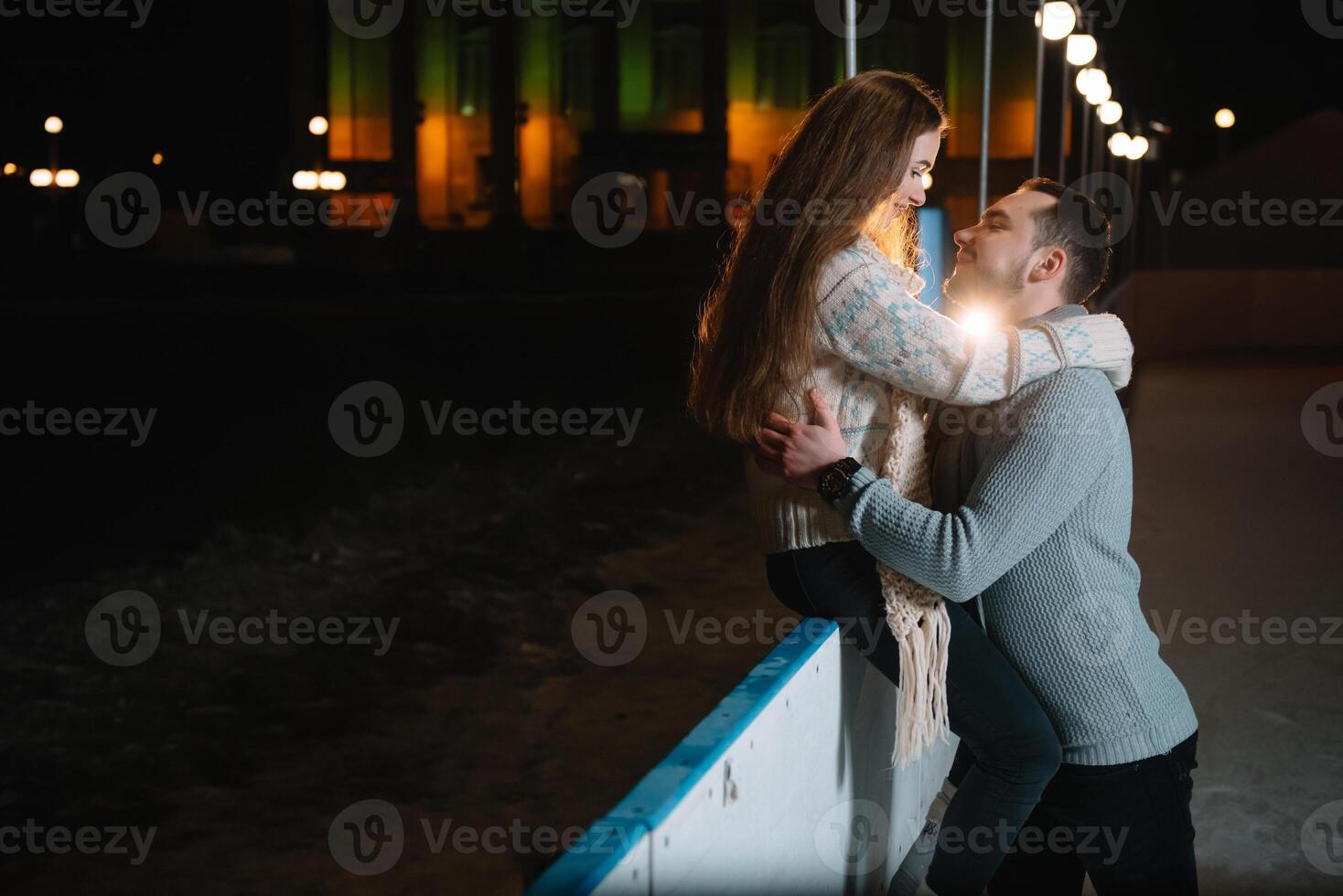 Theme ice skating rink and loving couple. meeting young, stylish people ride by hand in crowd on city skating rink lit by light bulbs and lights. Ice skating in winter for Christmas on ice arena. photo