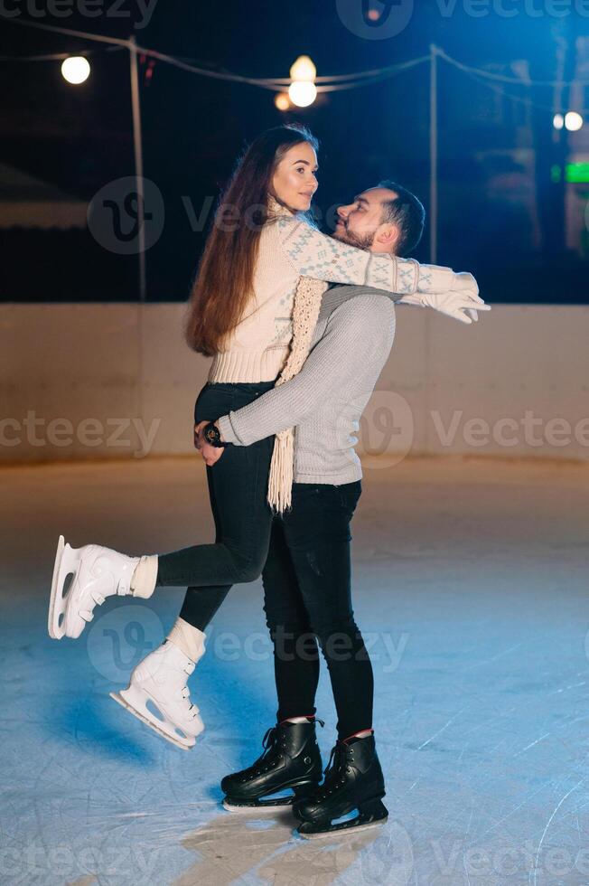 Theme ice skating rink and loving couple. meeting young, stylish people ride by hand in crowd on city skating rink lit by light bulbs and lights. Ice skating in winter for Christmas on ice arena. photo