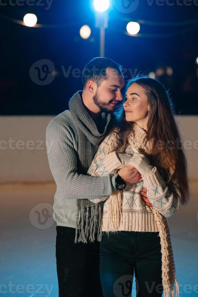 Theme ice skating rink and loving couple. meeting young, stylish people ride by hand in crowd on city skating rink lit by light bulbs and lights. Ice skating in winter for Christmas on ice arena. photo