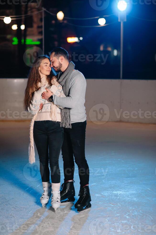 Theme ice skating rink and loving couple. meeting young, stylish people ride by hand in crowd on city skating rink lit by light bulbs and lights. Ice skating in winter for Christmas on ice arena. photo