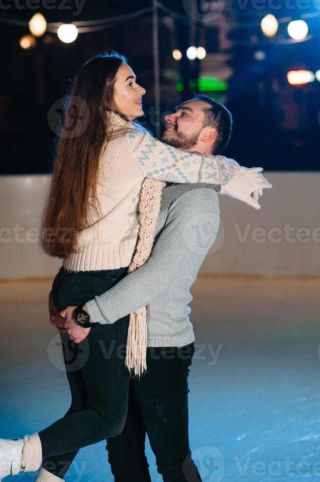 Theme ice skating rink and loving couple. meeting young, stylish people ride by hand in crowd on city skating rink lit by light bulbs and lights. Ice skating in winter for Christmas on ice arena. photo