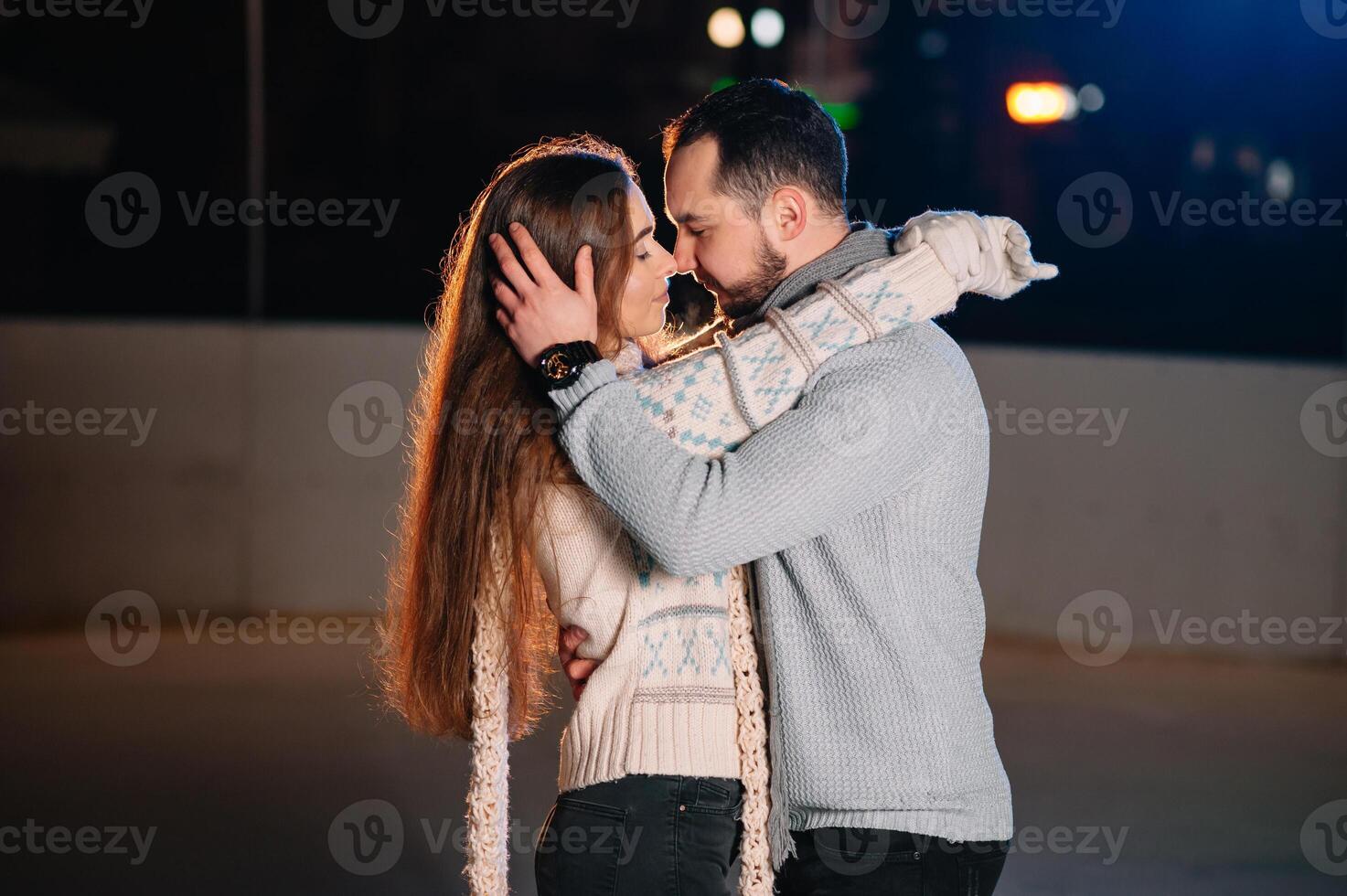 Theme ice skating rink and loving couple. meeting young, stylish people ride by hand in crowd on city skating rink lit by light bulbs and lights. Ice skating in winter for Christmas on ice arena. photo
