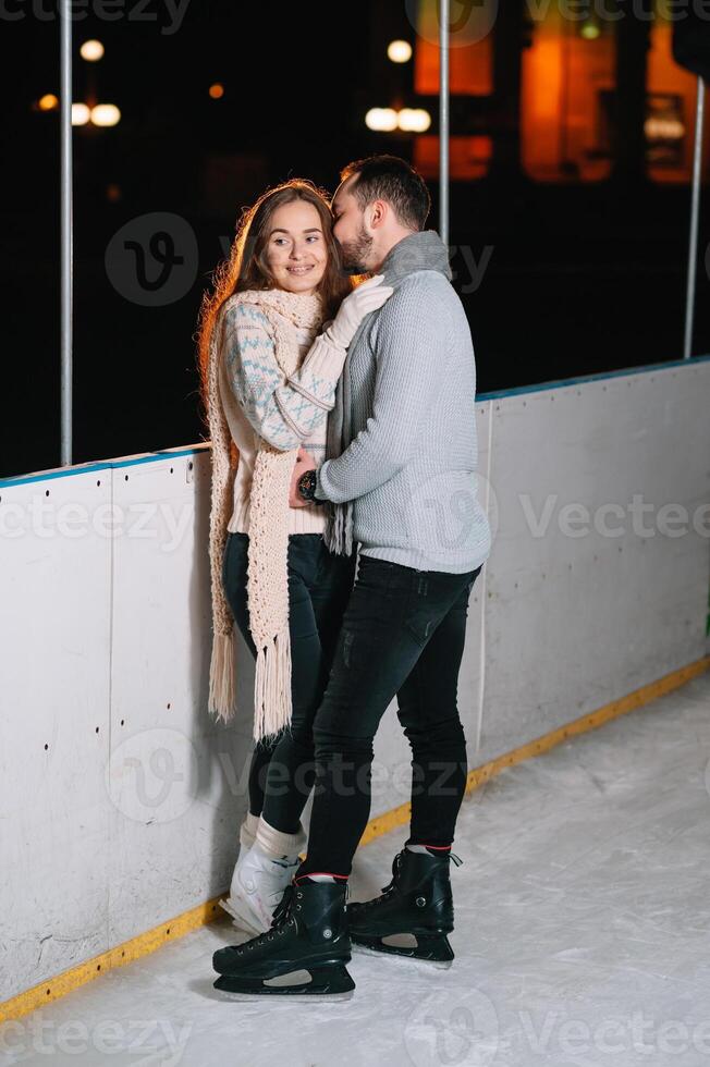 Theme ice skating rink and loving couple. meeting young, stylish people ride by hand in crowd on city skating rink lit by light bulbs and lights. Ice skating in winter for Christmas on ice arena. photo