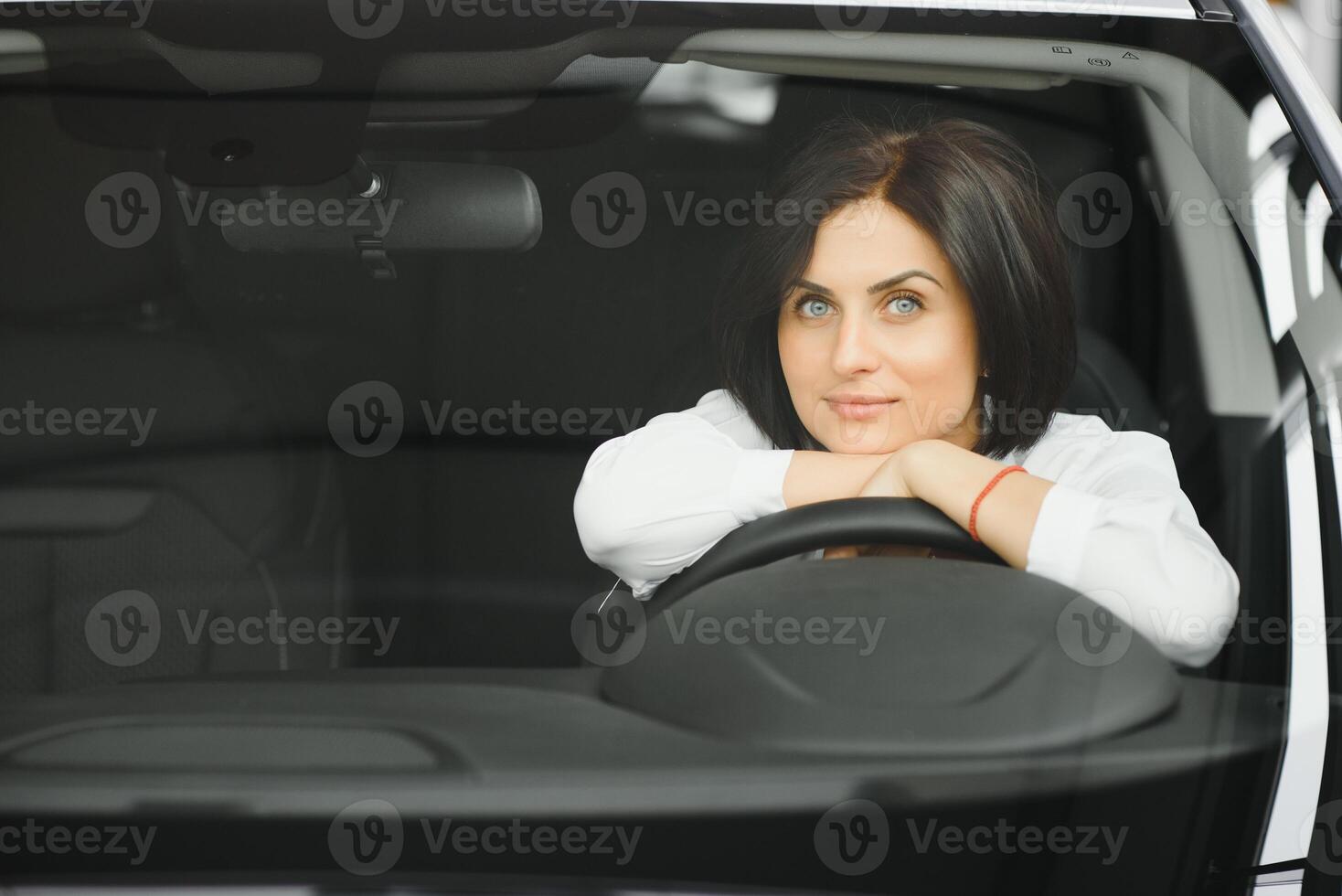 Young woman smiling in her new car in a showroom photo