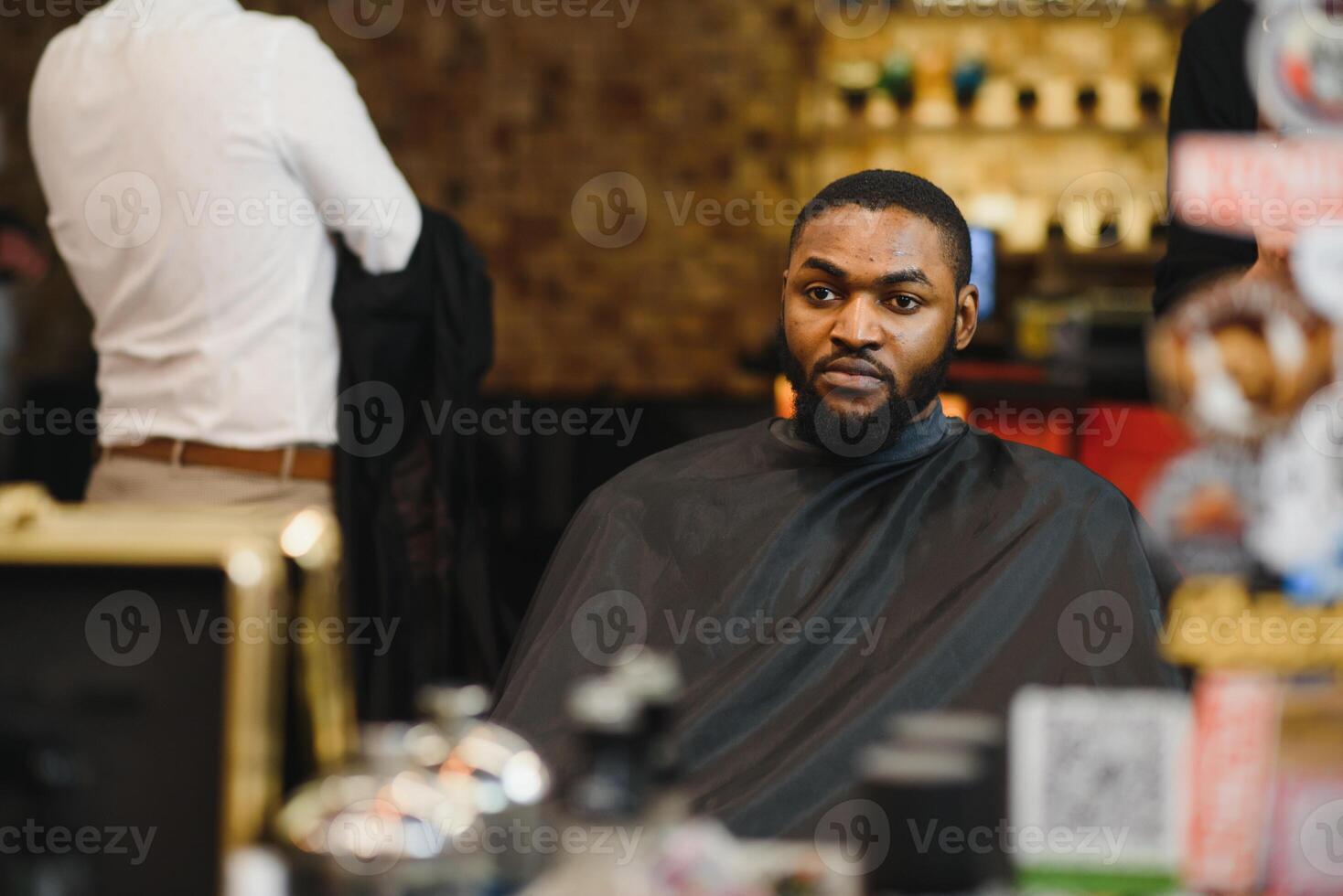 Side view of serious man with stylish modern haircut looking forward in barber shop. Hand of barber keeping straight razor and cutting trendy stripes on head of client. photo