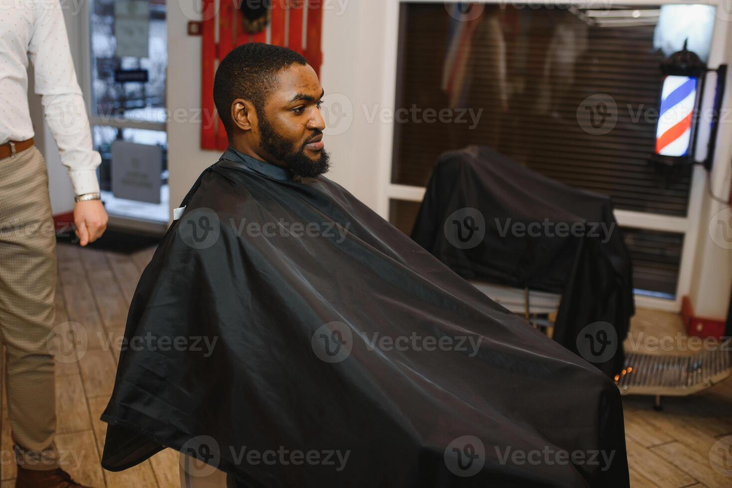 Portrait of young black man being trimmed with professional electric clipper machine in barbershop.Male beauty treatment concept. Young African guy getting new haircut in barber salon photo