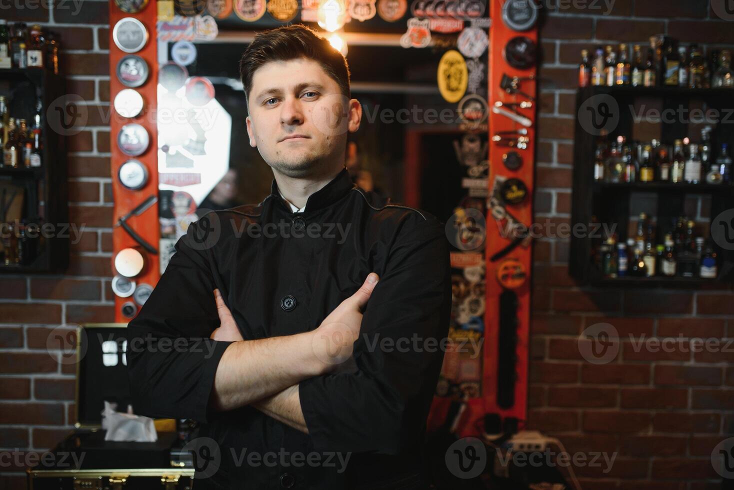 Portrait with copy space, empty place of virile harsh barber having his arms crossed, holding equipments in hand, looking at camera, isolated on grey background photo