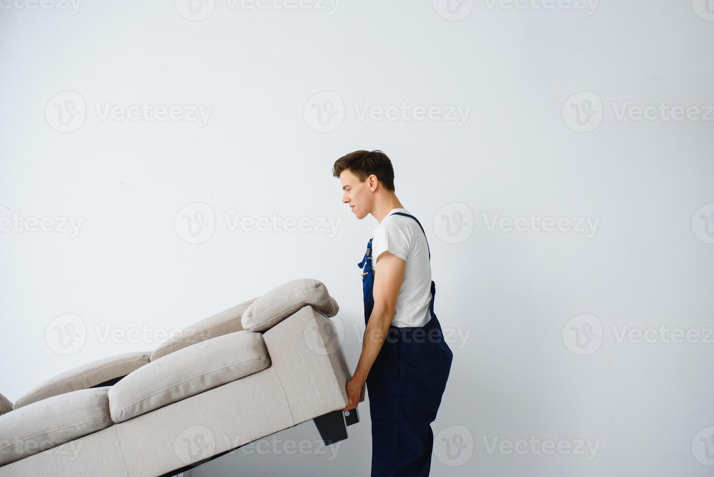 Loader moves sofa, couch. worker in overalls lifts up sofa, white background. Delivery service concept. Courier delivers furniture in case of move out, relocation. photo