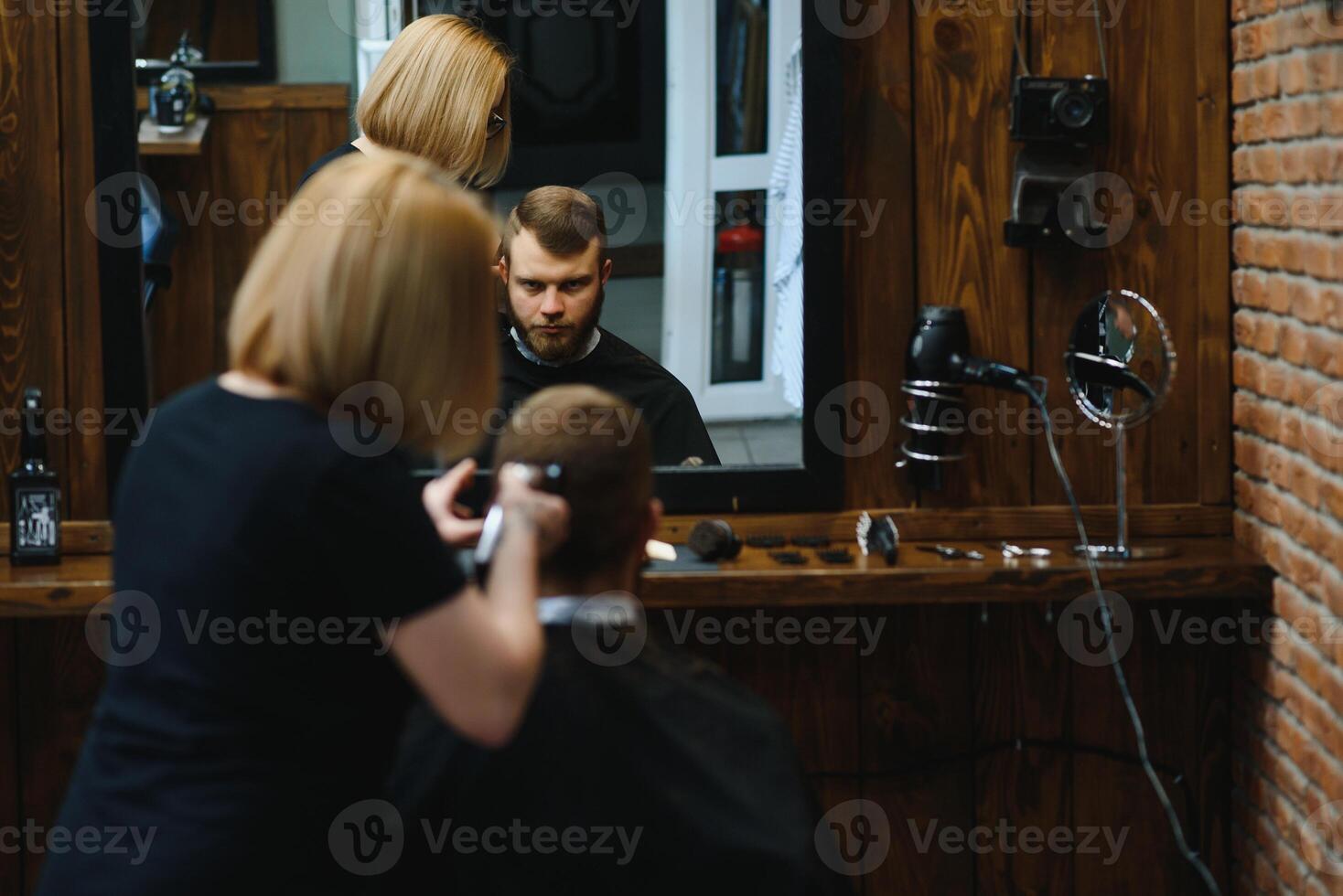 Stylish man sitting barber shop Hairstylist Hairdresser Woman cutting his hair Portrait handsome happy young bearded caucasian guy getting trendy haircut Attractive barber girl working serving client. photo
