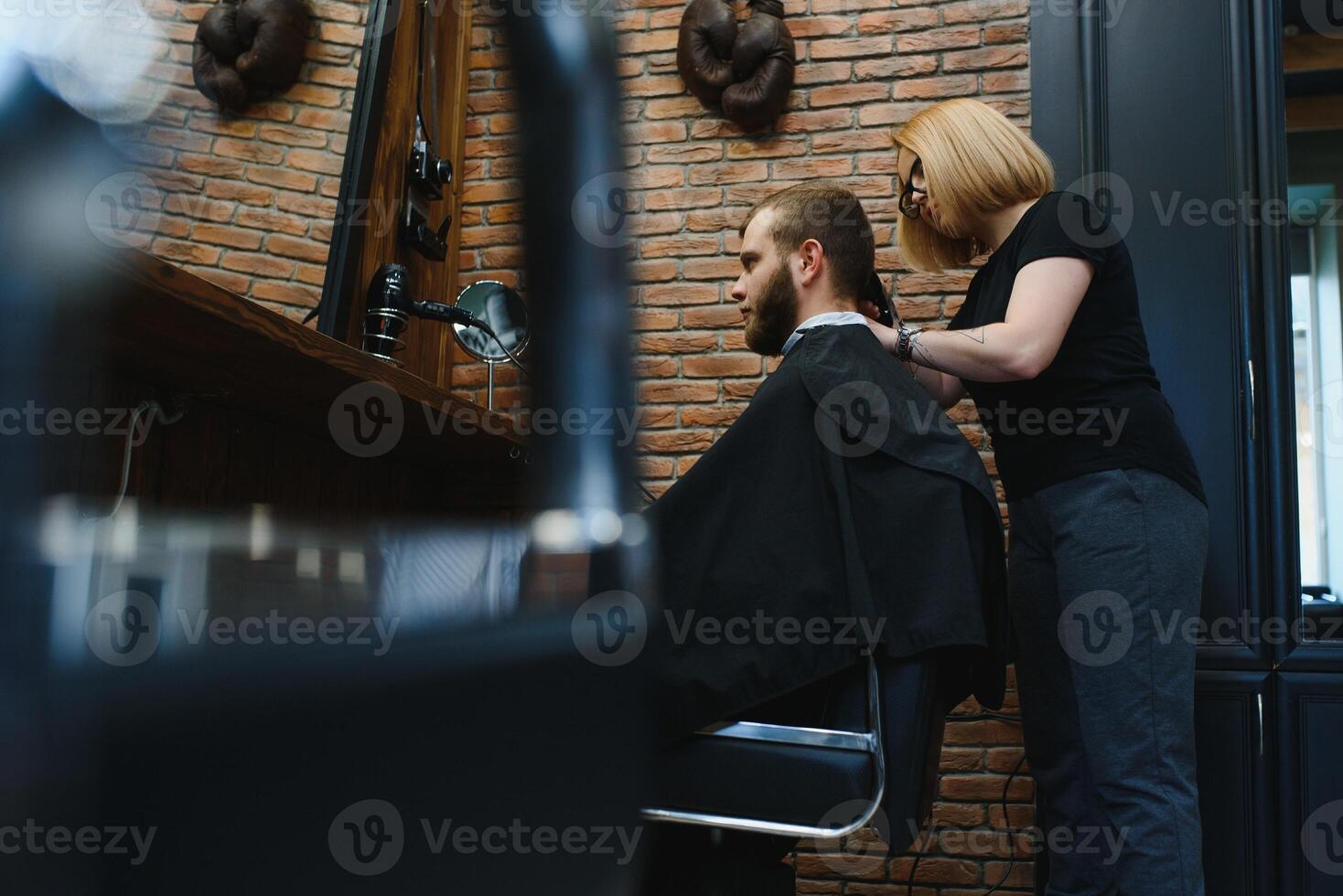 Stylish man sitting barber shop Hairstylist Hairdresser Woman cutting his hair Portrait handsome happy young bearded caucasian guy getting trendy haircut Attractive barber girl working serving client. photo