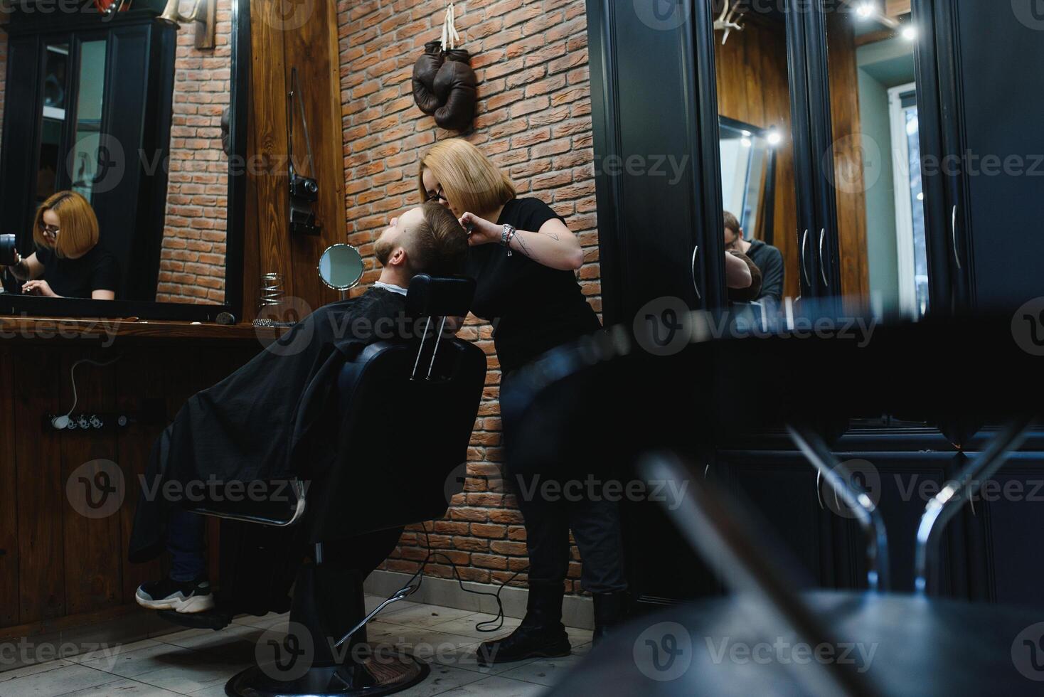 Young adult beautiful caucasian woman hairdresser cuts beard handsome man at modern barbershop Happy gay sitting chair men beauty salon. beard care. metrosexual. Female barber in black gloves serving photo