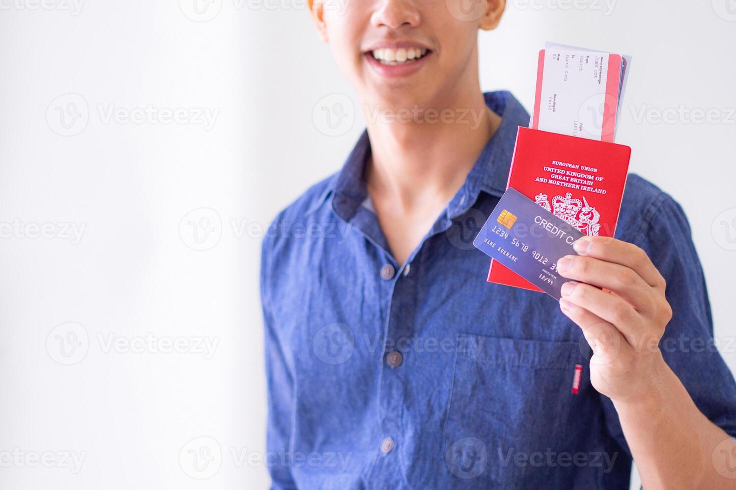 Young man wearing a blue shirt smiling and showing a blue credit card, passport, and plane ticket. Space for text. Concept of holiday and travel photo