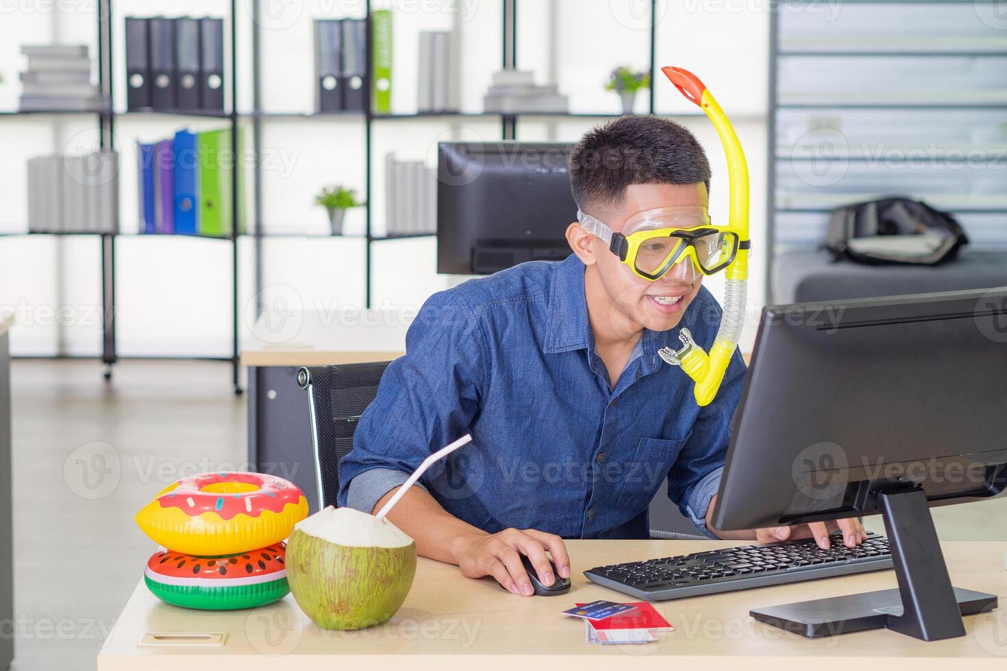 Young man wearing a diving mask yellow while sitting working in the office. He is dream of the sea because the holiday coming soon. Concept of people and holiday photo