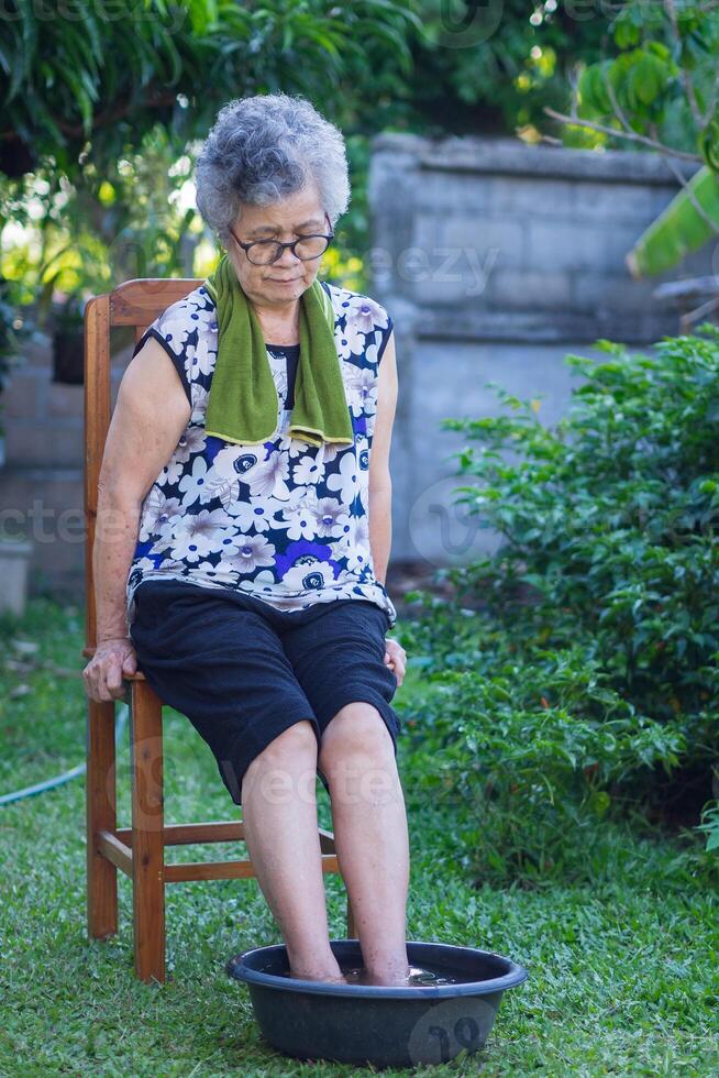 A senior woman has ankle pain and spa foot with herbs for relaxation treatment in the garden. Herbal treatment to relax the muscles by soaking warm water that is boiled from herbs photo