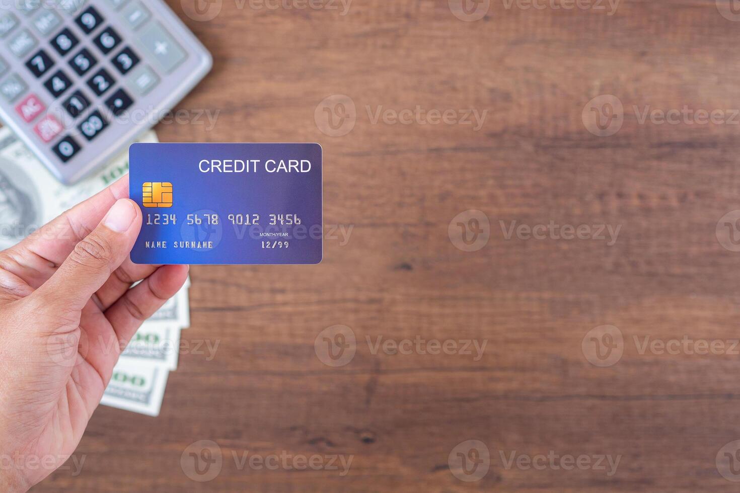 Close-up of hand holding a credit card with money US dollars background and a calculator placed on a wooden table. Space for text. Concept of business, e-commerce, and payment photo