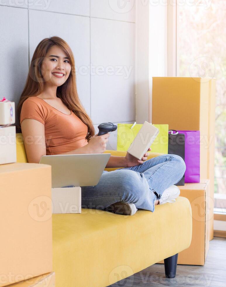 Asian businesswoman is an e-commerce entrepreneur sitting on a chair, smile and looking at the camera, the right hand holding the barcode reader and the left hand holding the parcel box photo