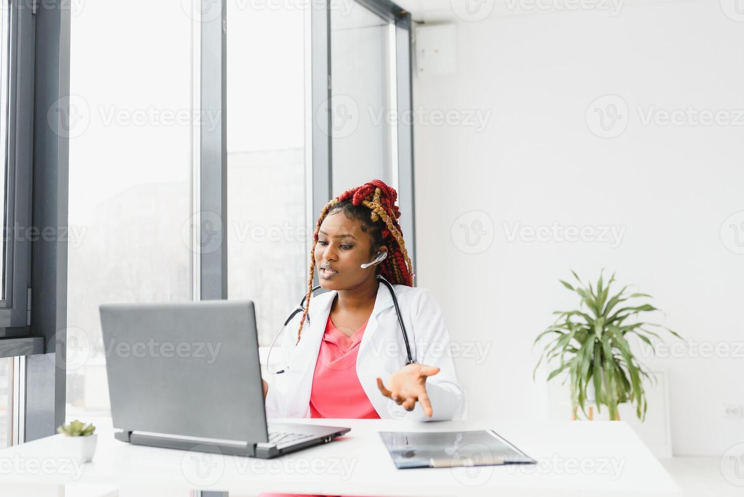 medicine, online service and healthcare concept - happy smiling african american female doctor or nurse with headset and laptop having conference or call at hospital. photo