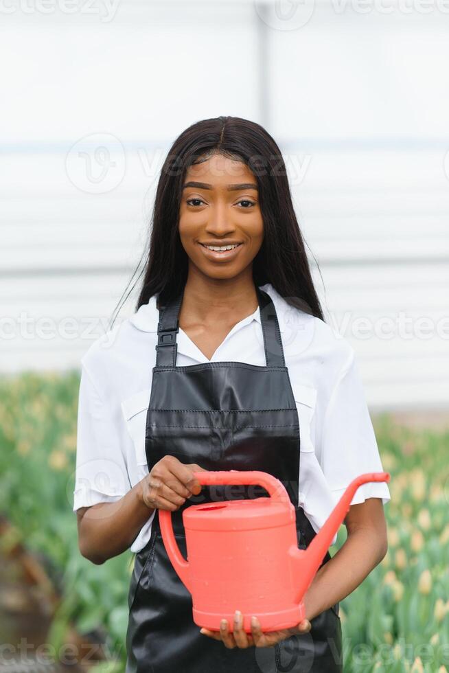 Beautiful young smiling african american girl, worker with flowers in greenhouse. Concept work in the greenhouse, flowers. photo