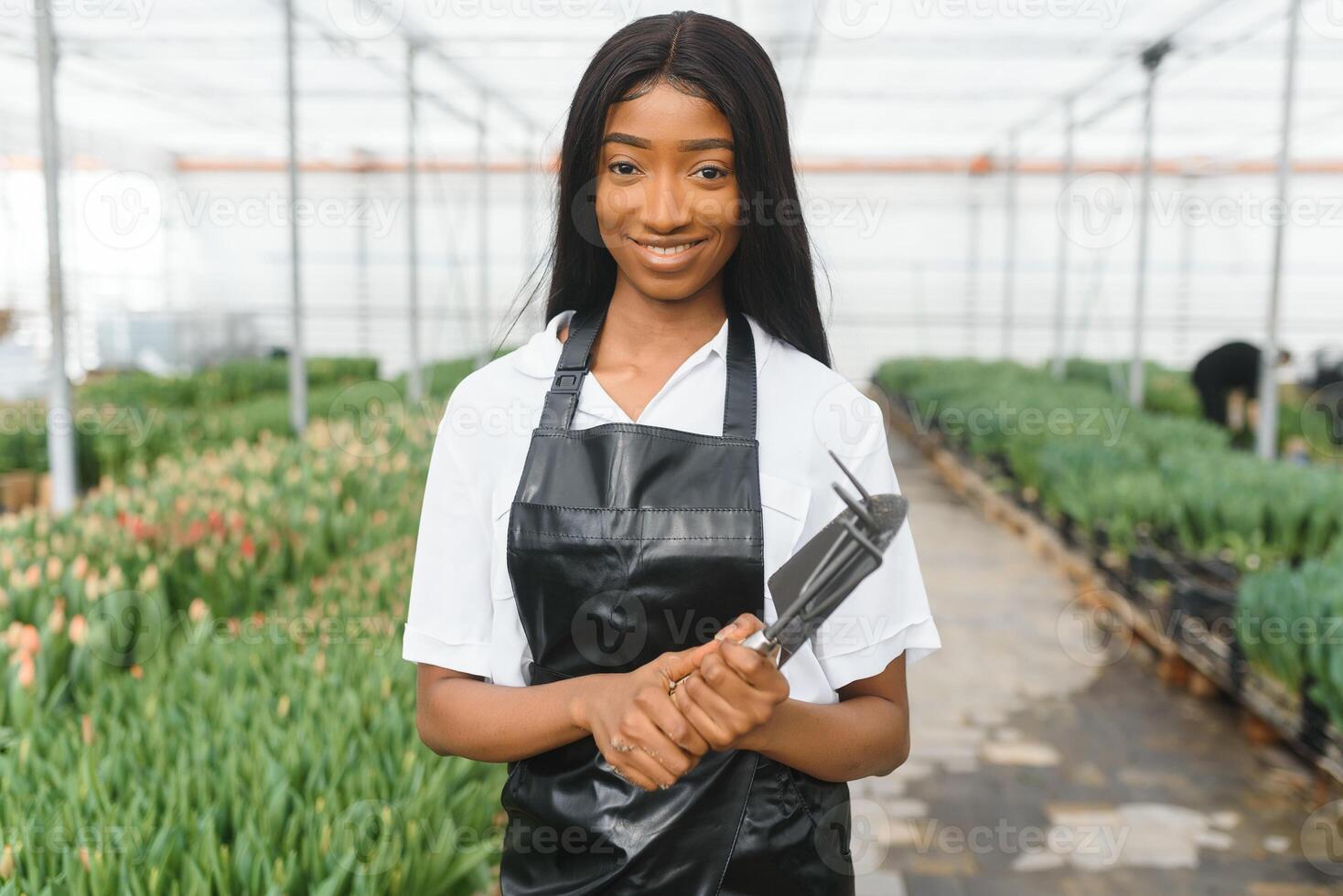 Beautiful young smiling african american girl, worker with flowers in greenhouse. Concept work in the greenhouse, flowers. photo