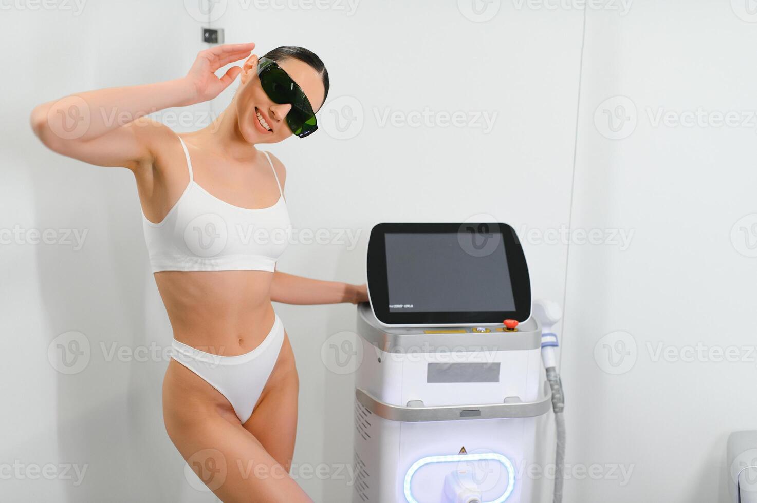 Young beautiful woman with laser hair removal machine in cosmetology cabinet photo