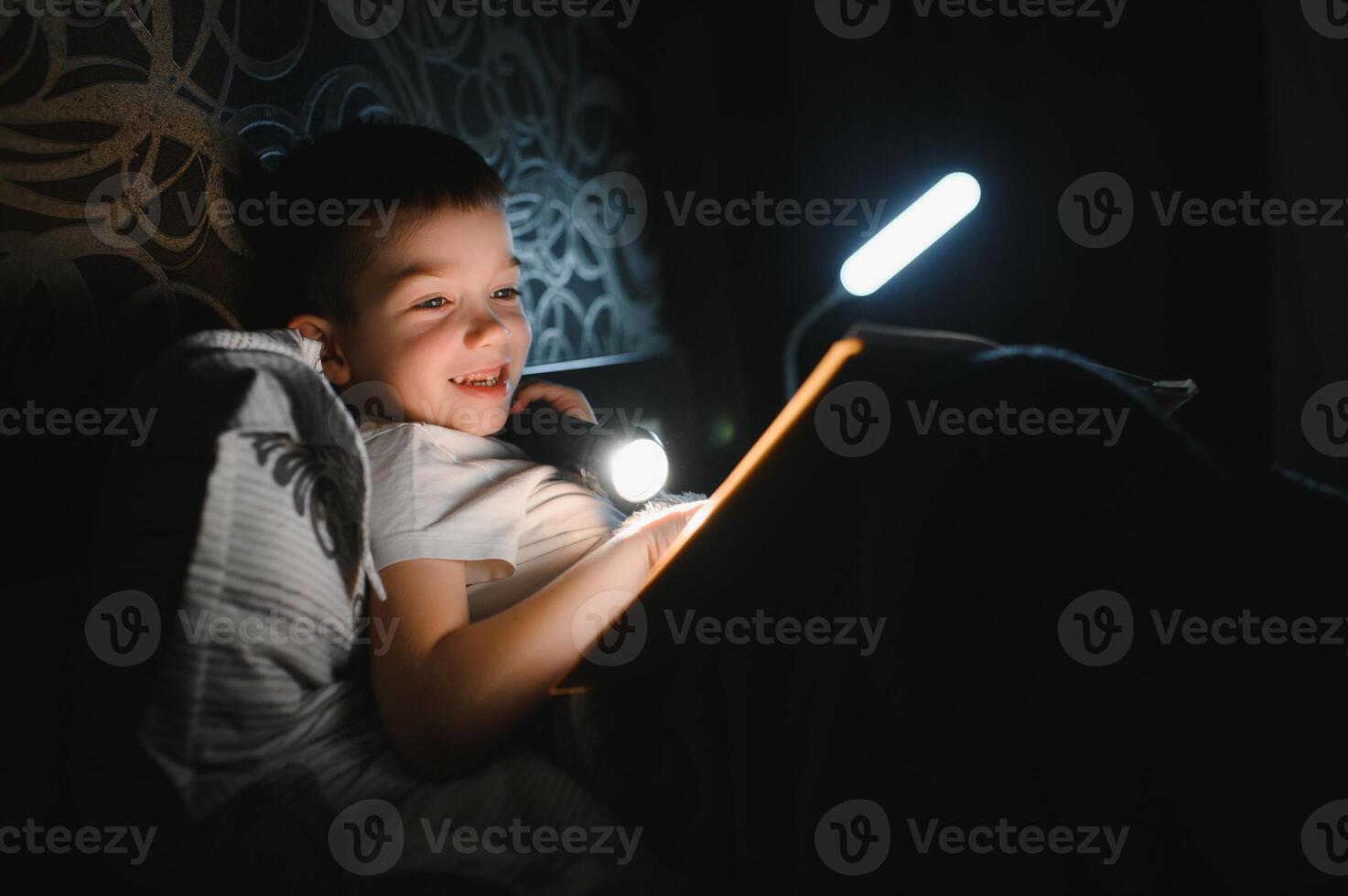 Child reading book in bed. Kids read at night. Little boy with fairy tale books in bedroom . Education for young children. Bedtime story in the evening. Cute kid under blanket in dark room with lamp photo