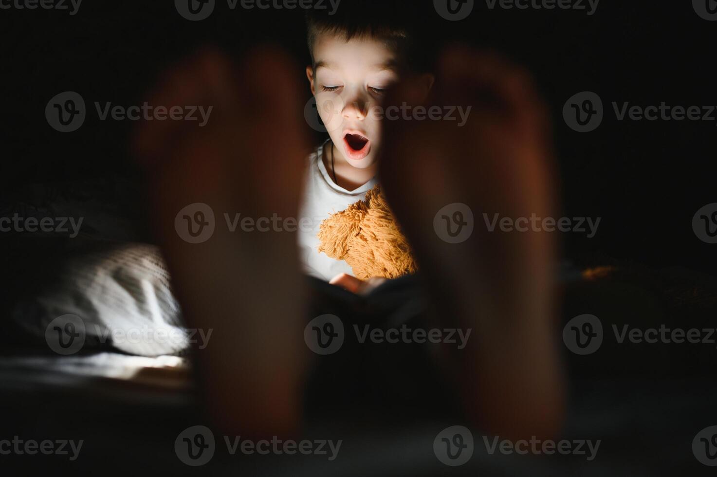 Reading book and using flashlight. Young boy in casual clothes lying down near tent at evening time photo