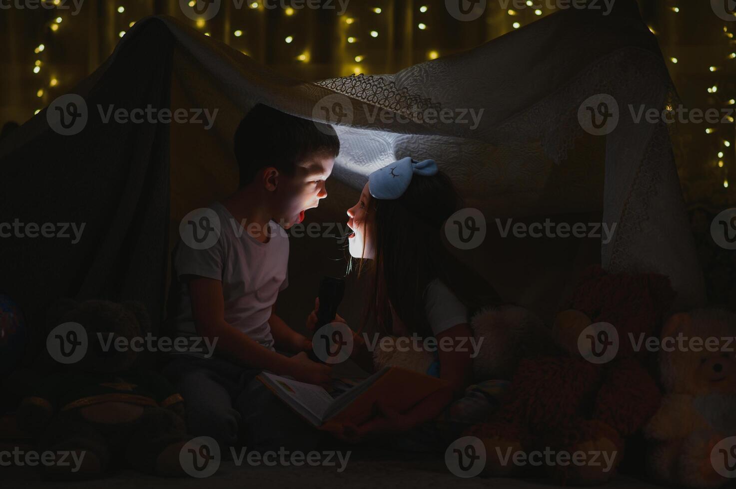 children boy and girl playing and frighten each other with flashlight in tent at night photo