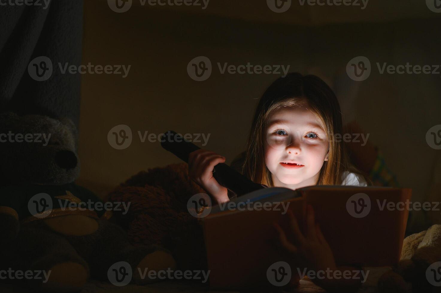 Reading and family games in children's tent. Little girl with books and flashlight before going to bed. photo