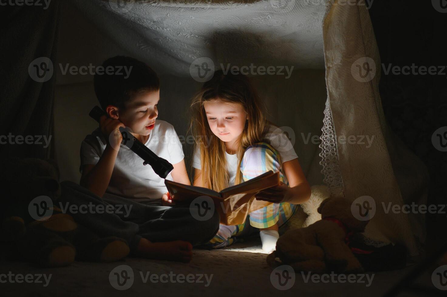happy family children reading a book with a flashlight in a tent at home photo