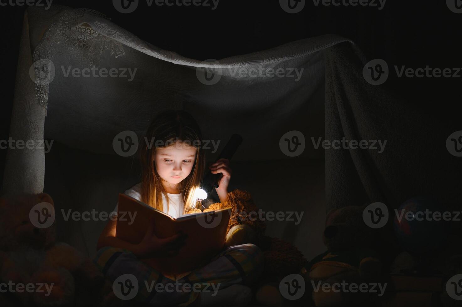 Little girl are reading a book with flashlights in tent. Happy girl playing at home. Funny lovely kid having fun in room. photo