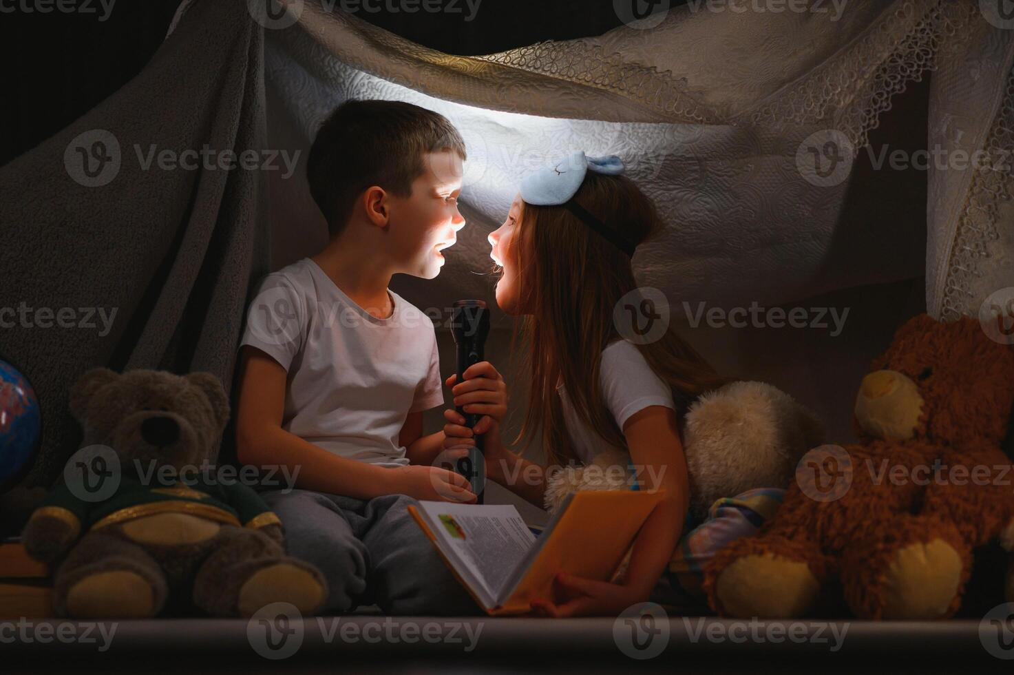 Two little child play at home in the evening to build a camping tent to read books with a flashlight and sleep inside. photo