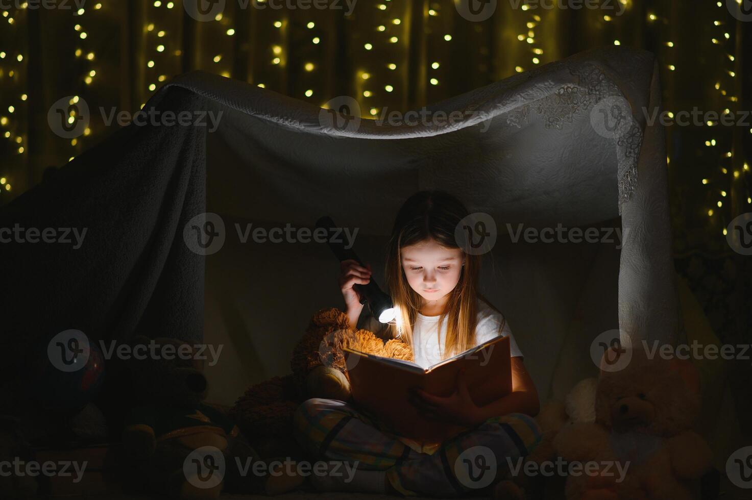 happy child girl laughing and reading book in dark in a tent at home photo