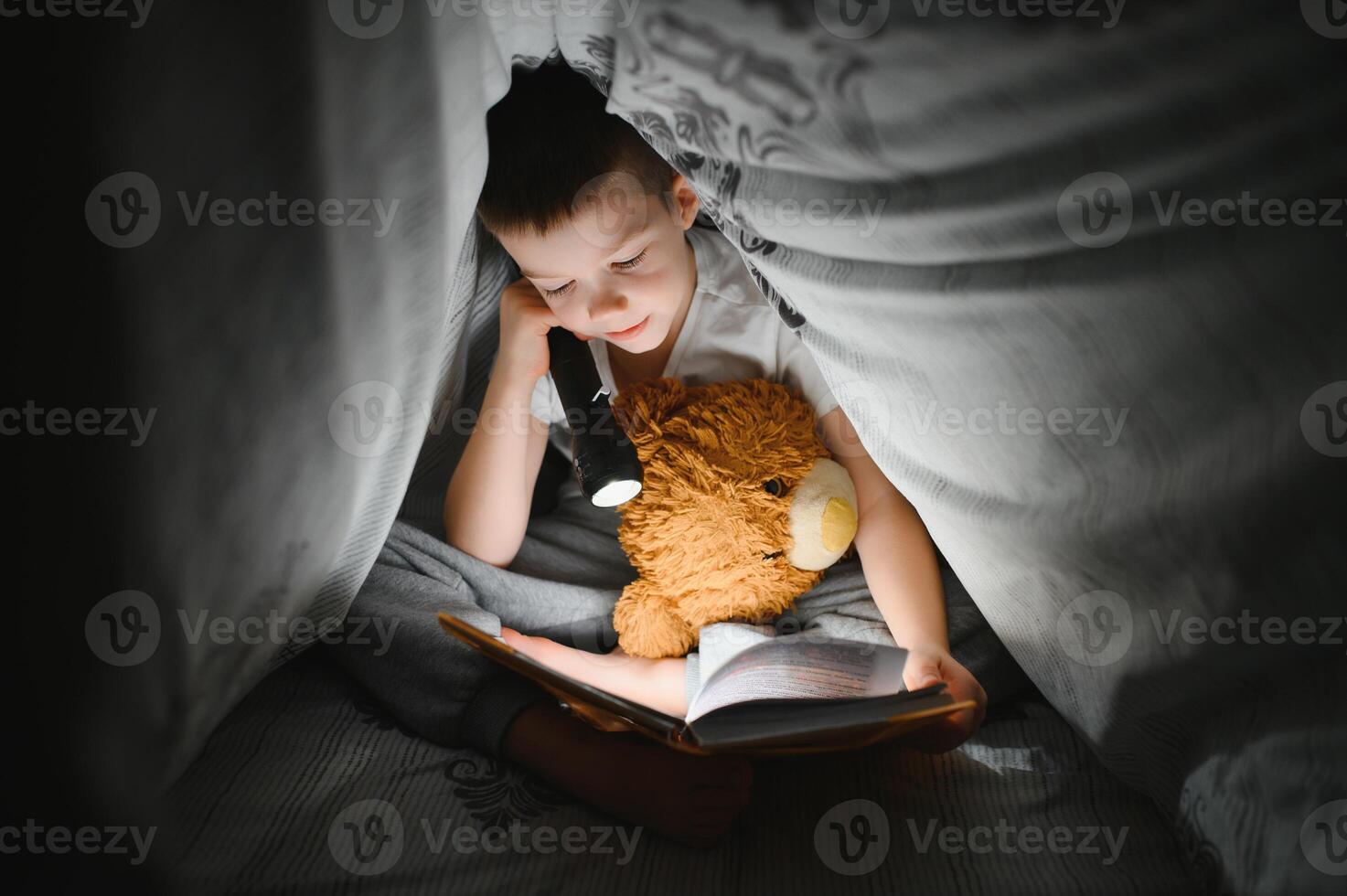 Reading book and using flashlight. Young boy in casual clothes lying down near tent at evening time photo